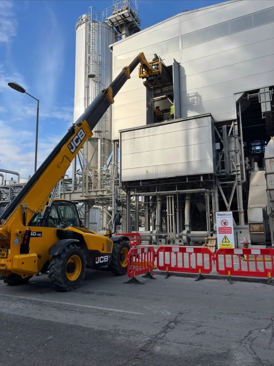 A telehandler positioned alongside exterior silo and conveyor structures to provide access.