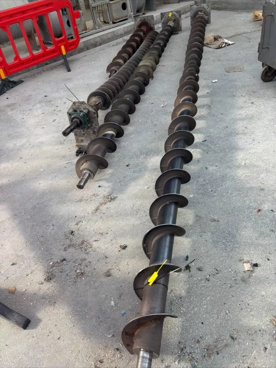 Three conveyor screw assemblies laid out on the floor for inspection before replacement.