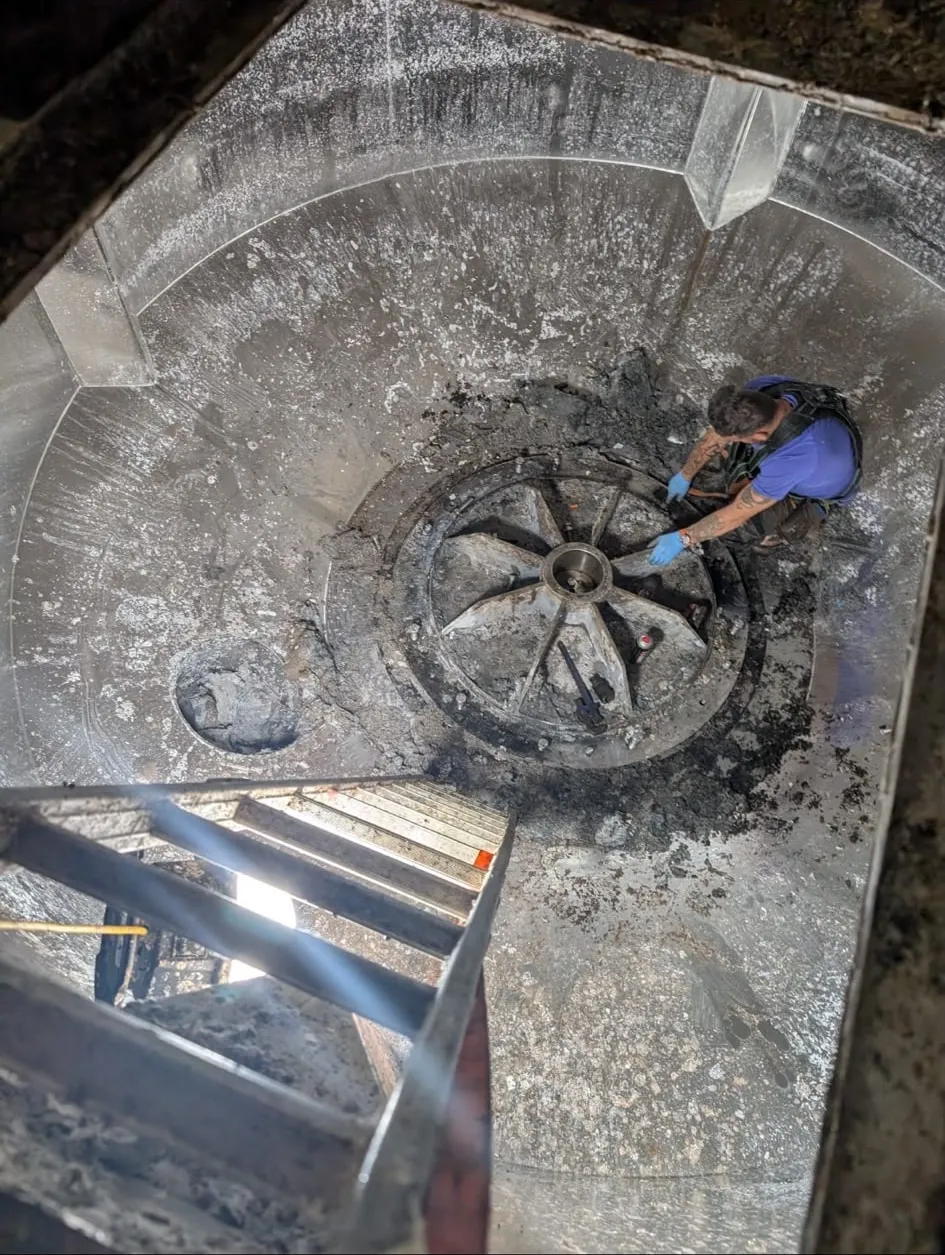 A technician inspecting a broke pulper rotor from above, the vessel wall heavily coated with pulp residue.