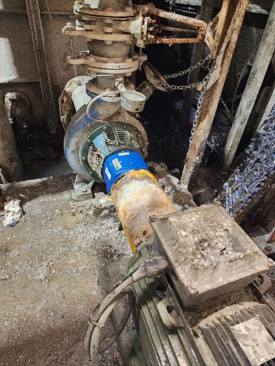 A pump and motor set installed in a plant pit with the coupling guard fitted and a chain hoist rigged above.