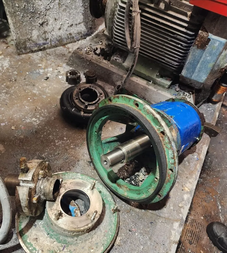 A pump stripped down beside its motor, with the casing ring, impeller, machined shaft, seal housing and coupling laid out on the floor.