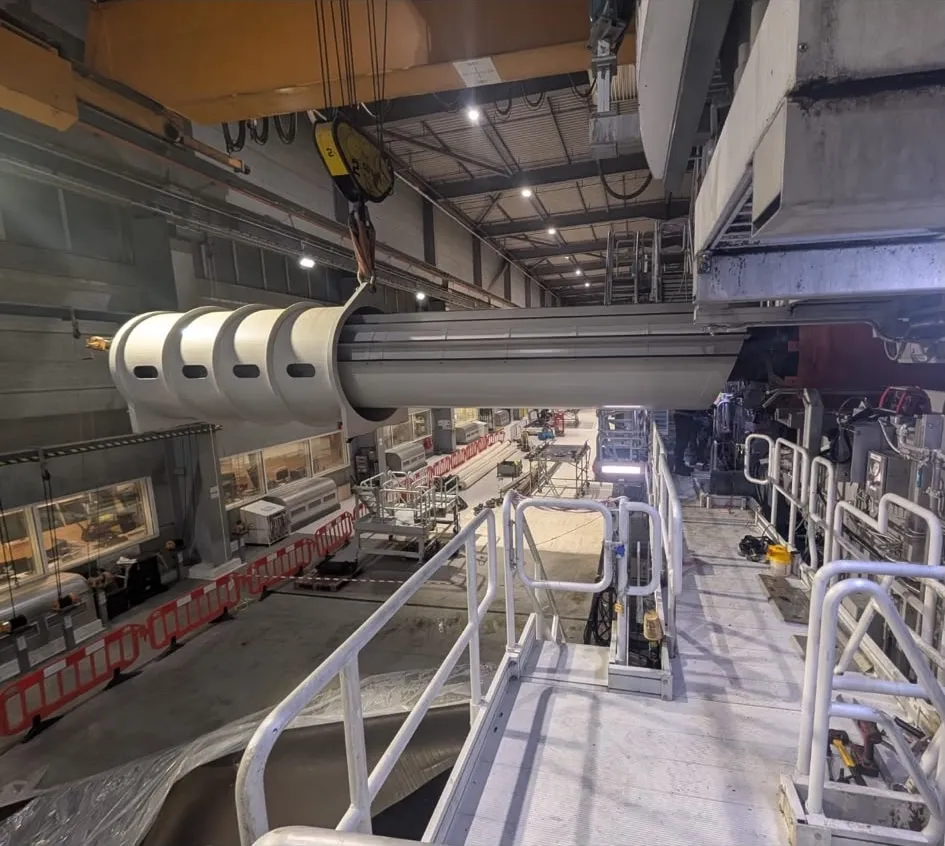 A replacement machine roll wrapped in protective sheeting and suspended for positioning.