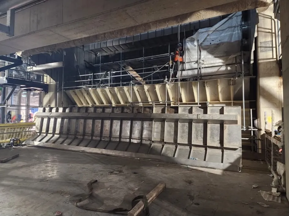 A large fabricated stainless steel vessel under installation on a plant floor, with access steelwork around it.